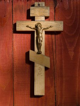Small wooden crucifix hanging on wooden wall under beam of light