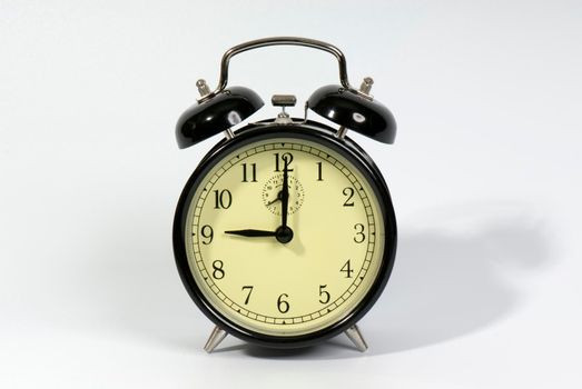 Old fashioned alarm clock showing 9 o'clock on a white background