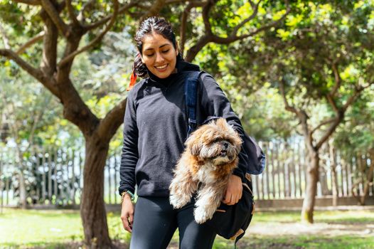 A charming young woman walks in nature, with a backpack on her shoulder, from which her dog peeks out. Concept relationship and love towards animals