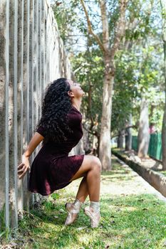 Beautiful young graceful ballerina in black dress sitting and on tiptoe in park looking up