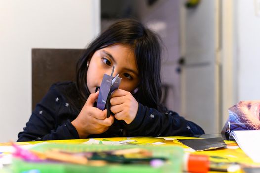 little girl cutting paper with scissors for homework