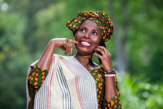 young african woman standing in traditional dress on mobile phone looking up laughing.