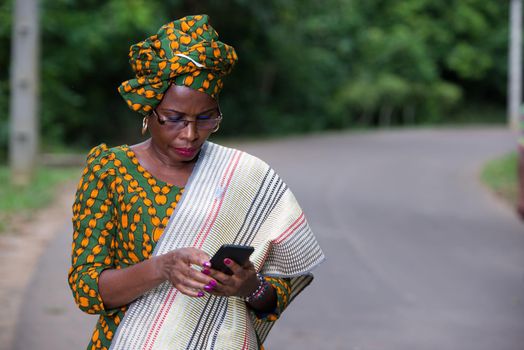 young african woman standing in loincloth and glasses looking at mobile phone.