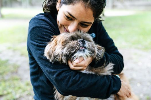 Cute young woman is kissing and hugging her little puppy. Love between owner and dog. Outdoor photo in the park, selective focus. Lifestyle concept