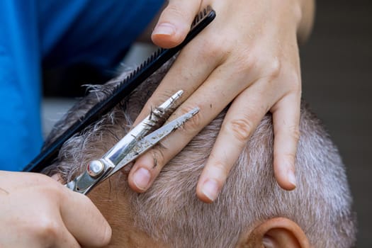 Hands of a professional barber with scissors and comb combs the hair of a man haircut for a client at a men