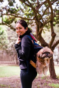 A charming young woman walks in nature, with a backpack on her shoulder, from which her dog peeks out. Concept relationship and love towards animals