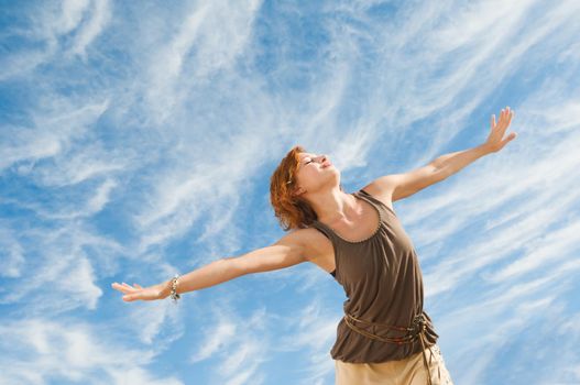 Beautiful young dancer performing yoga-dance outdoors with blue sky and clouds in the background