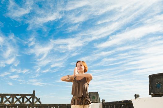 Beautiful young dancer performing yoga-dance outdoors with blue sky and clouds in the background