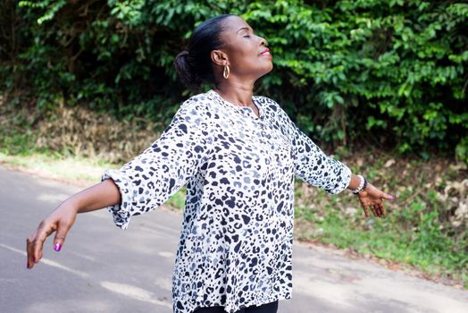 young lady standing in black white shirt with outstretched arms breathing fresh air smiling with eyes closed.