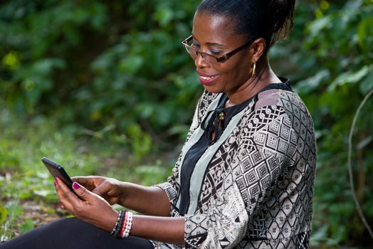 Beautiful woman resting in the forest speaks by mobile phone sitting at the park in casual clothes. Close up of big greenery in the park and holding the smart phone. technology and communication concept