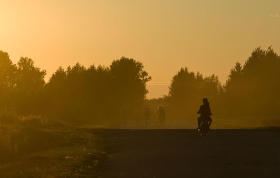 Golden sunset. Two boys riding a small bike and three girls on a bicycles