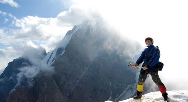 Young mountaineer is standing at the very edge of a rocky mountain top. Behind him is the sun shining right throung the cloud creating great lighting effect