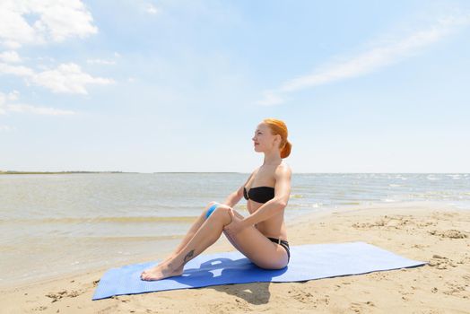 Beautiful slim woman wearing bikini exercising with fit ball on yoga mat at the beach