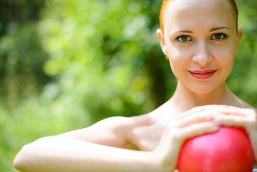 Beautiful red woman exercising in green park with fit ball