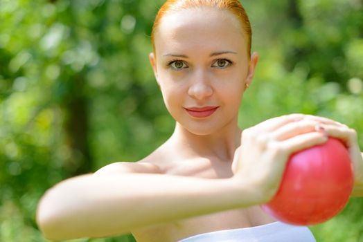 Beautiful red woman exercising in green park with fit ball