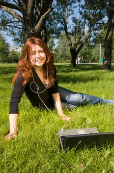 Beautiful girl listening to the music from her laptop in the park