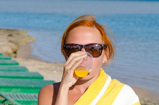 Red woman wearing sunglasses drinking orange juice