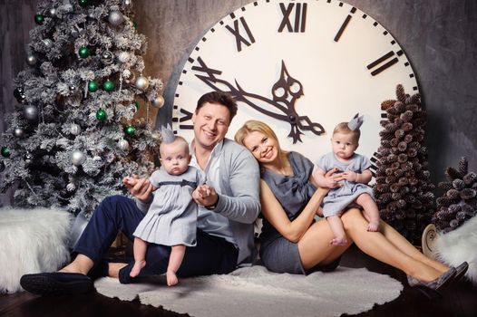 A happy big family with twin children in the New Year's interior of the house against the background of a large clock.