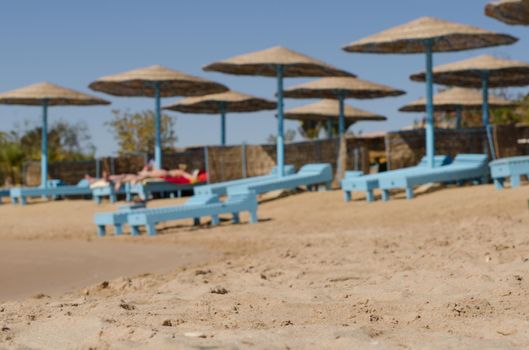 Beach with sunbeds and umbrellas. Very shallow depth of field with focus on sand. People blurred in the background
