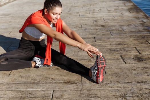 Outdoor shot of fit and healthy sportswoman stretching her legs and workout along seaside promenade.