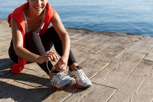 Cropped shot of athlete woman tying shoelaces during workout near sea.