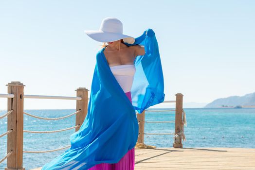 Photo of beautiful young woman wearing hat and blue veil at sea resort