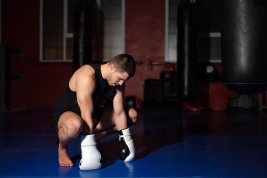 Kickboxing fighter in boxing gloves standing on knees. High quality photo