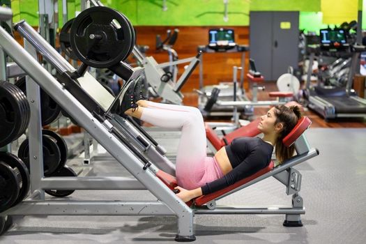 Side view of fit young sportswoman flexing her leg's muscles on exercise machine at the gym. High quality photo.