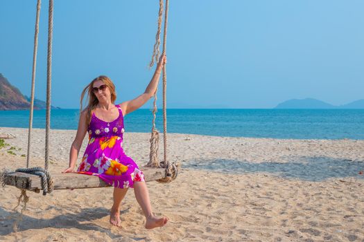 Young woman swinging on a swing suspended from a palm tree on the seashore. Travel and tourism to the tropical countries of Asia.