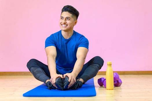 Young Hispanic man practicing yoga on his mat at gym on pink background. High quality photo