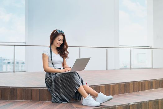 Smiling pretty female entrepreneur working on laptop outdoors