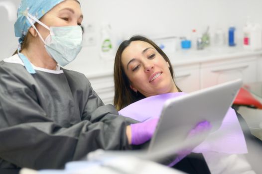 Health care concept - Female dentist showing tablet computer to woman patient at dental clinic office. High quality photo