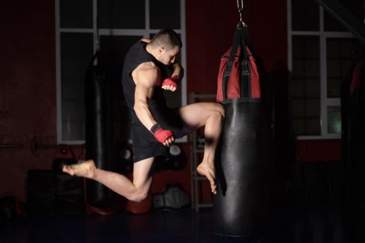 Kickboxing fighter Performing Jumping Air Kicks with Knee on Punch Bag. Caucasian Man Practicing Martial Arts Training at Urban Gym. High quality photo.