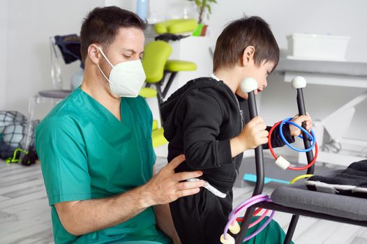 Child with cerebral palsy on physiotherapy in a children therapy center. Boy with disability doing exercises with physiotherapists in rehabitation centre. High quality photo.