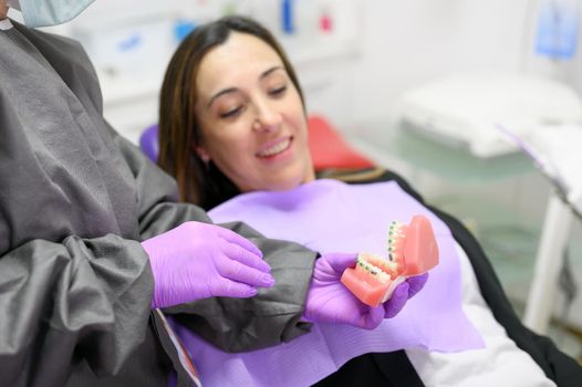 Dentist showing to patient an orthodontics dental model, explaining to patient the orthodontics treatment in dental clinic. High quality photo