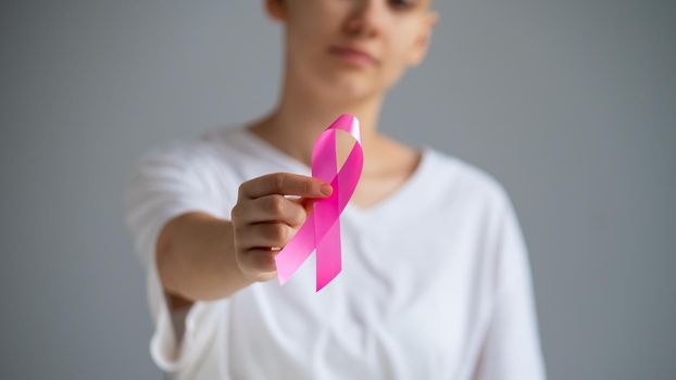 A faceless woman wearing a white t-shirt holds a pink ribbon as a symbol of breast cancer on a white background