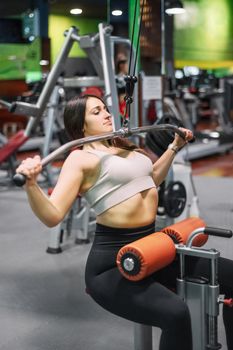 Young sportswoman exercising on lat machine in gym. High quality photo