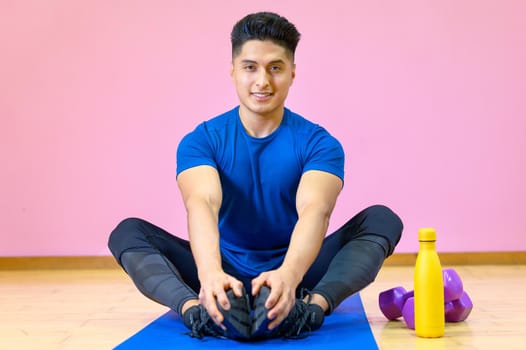 Young Hispanic man practicing yoga on his mat at gym on pink background. High quality photo