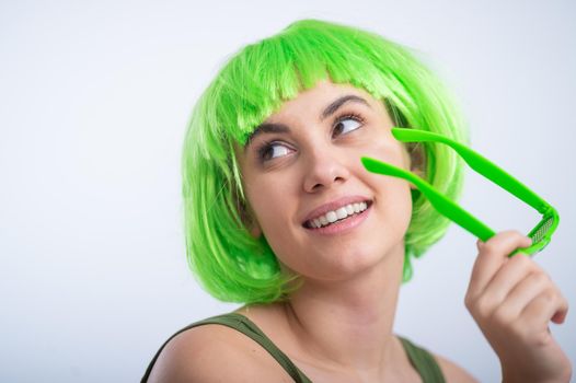 Cheerful young woman in green wig and funny glasses celebrating st patrick's day on a white background.