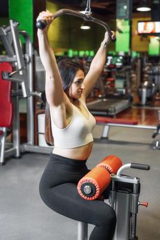 Young sportswoman exercising on lat machine in gym. High quality photo