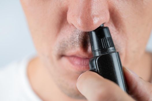 A man cuts his nose hair with a pocket trimmer.