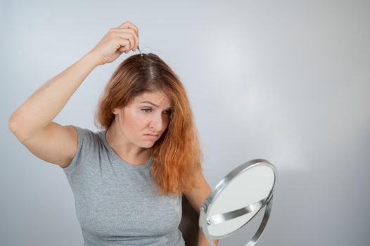 Caucasian woman finds gray hair and removes it with tweezers. Signs of aging