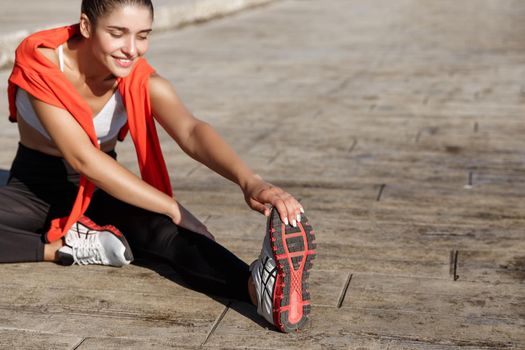 Outdoor shot of fit and healthy sportswoman stretching her legs and workout along seaside promenade.