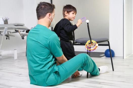 Child with cerebral palsy on physiotherapy in a children therapy center. Boy with disability doing exercises with physiotherapists in rehabitation centre. High quality photo.