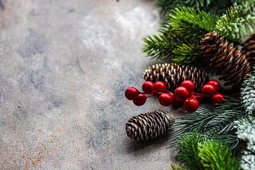Christmas card concept with frame made with green fir branches, red decoration balls and berries on concrete background