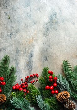 Christmas card concept with frame made with green fir branches, red decoration balls and berries on concrete background