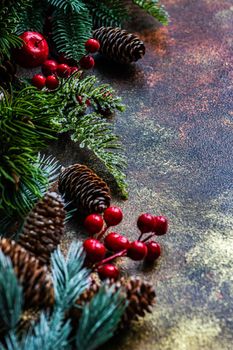 Christmas card concept with frame made with green fir branches, red decoration balls and berries on concrete background