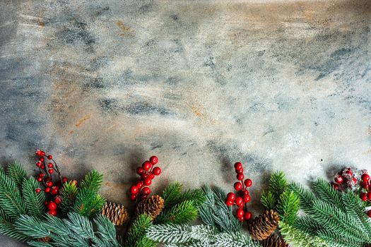 Christmas card concept with frame made with green fir branches, red decoration balls and berries on concrete background