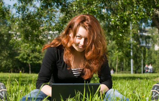 Young red haired student hangs out in a park with her laptop