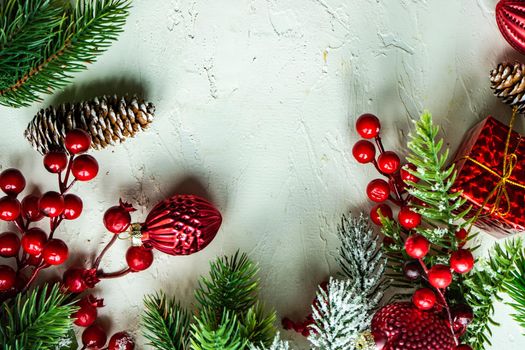 Christmas card concept with frame made with green fir branches, red decoration balls and berries on concrete background